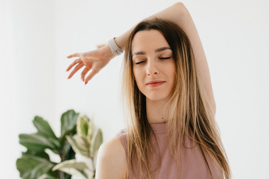 woman in peach top, with her eyes closed, thinking of positive health affirmations