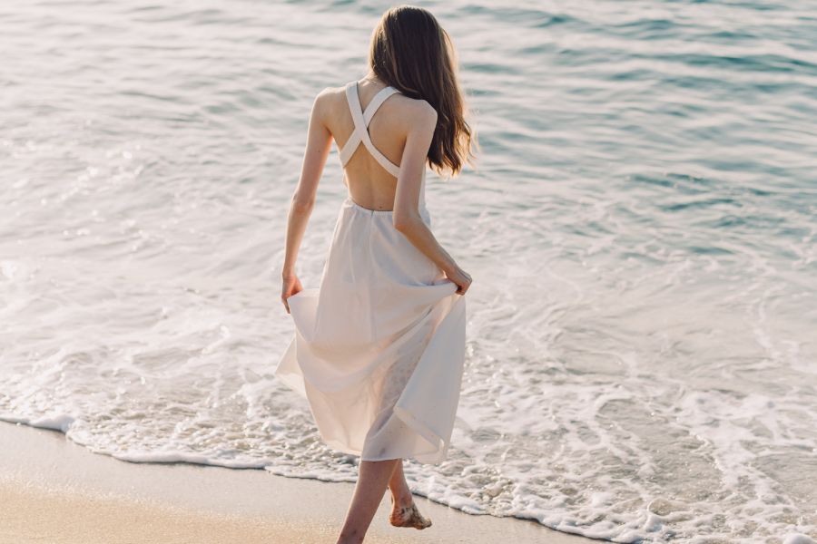 woman in white summer dress, entering sea barefoot, letting go of feeling guilty about self-care