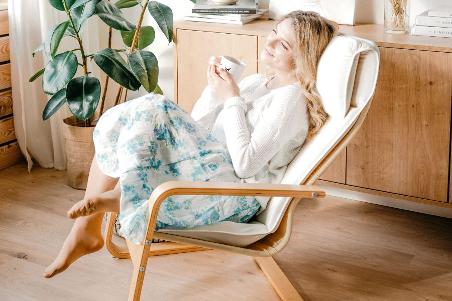 girl drinking coffee on a recliner, wearing blue dress and white cardigan, thinking of ways to slow down