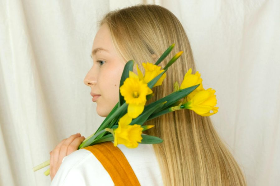 woman in orange jumpsuit holding yellow flowers practicing self-love habits