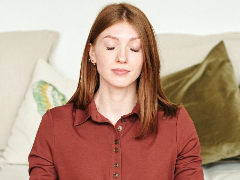 Woman in orange top, meditating while smiling, making use of 5-minute self-care activities