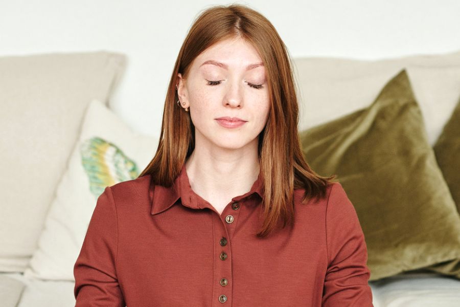 Woman in orange top, meditating while smiling, making use of 5-minute self-care activities