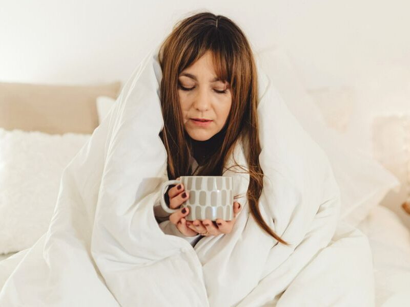 woman wrapped in a white blanket drinking tea to stop being sad
