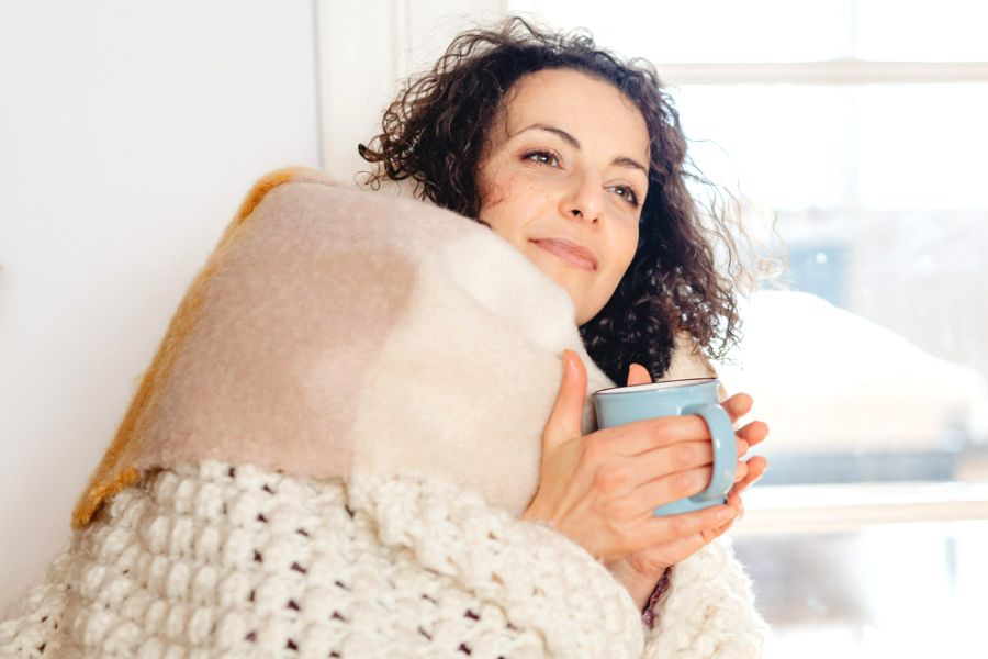 woman wrapped in a quilt holding a blue coffee mug, thinking about habits of people who never get stressed
