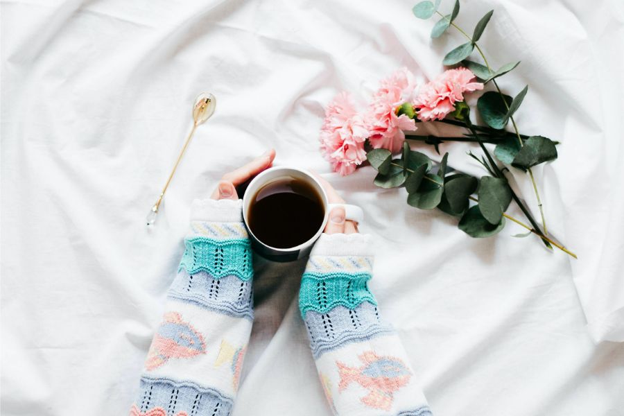 hand holding a mug of coffee, with flowers on bed, as part of a 5am morning routine