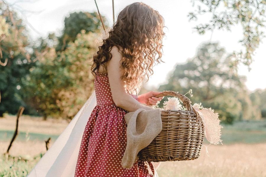 woman in a red dress, holding a basket of flowers in a green field, looking for ways to be a better person 