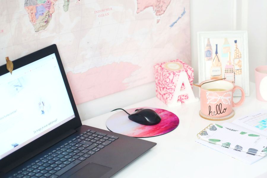 laptop, hello coffee mug, mouse pad with black mouse, a notebook on white table (girl boss habits)