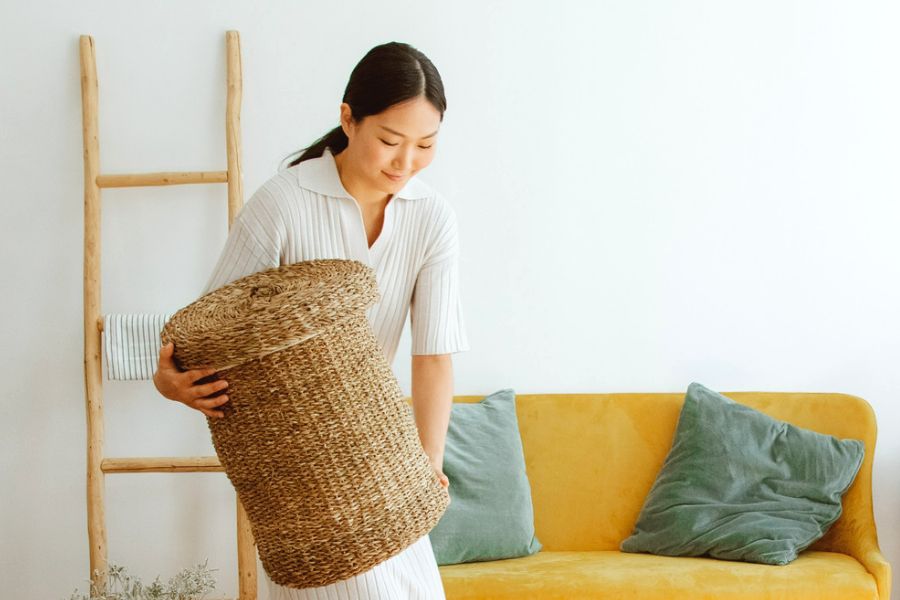 smiling asian woman carrying a laundry basket made of jute, practicing habits of organized people