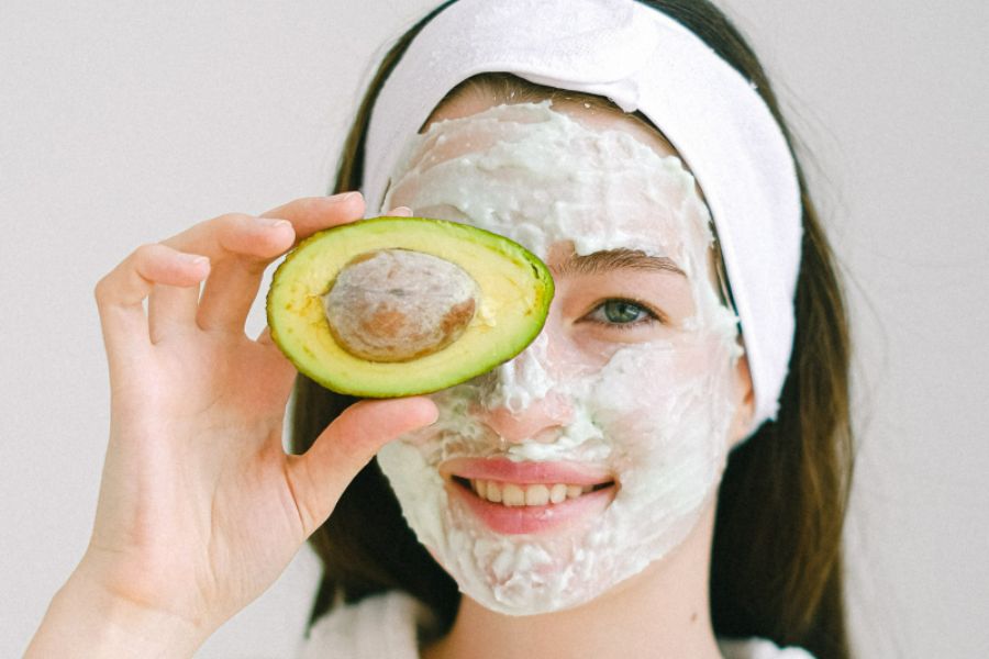 that girl wearing face mask holding an avocado while smiling