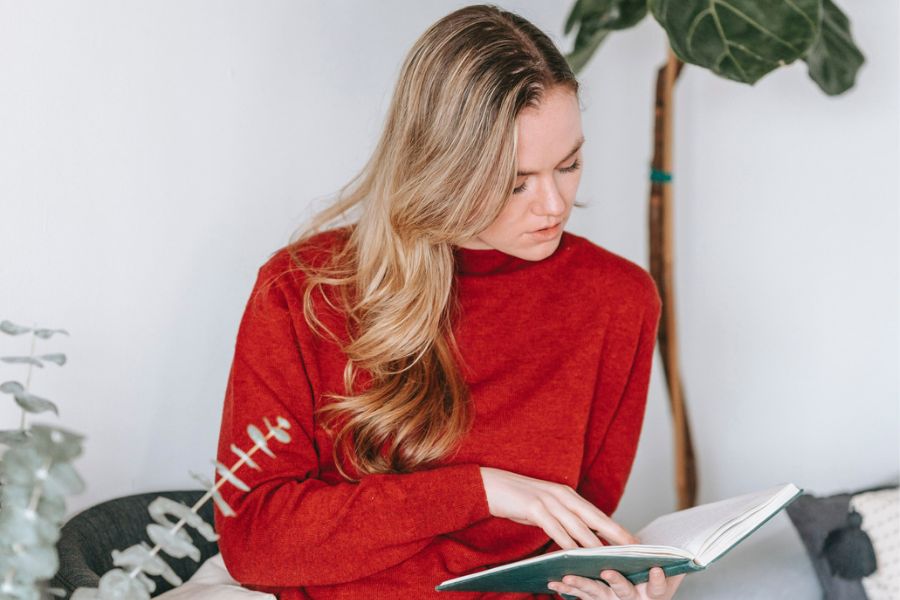woman wearing red sweater reading a book, practicing Sunday habits 
