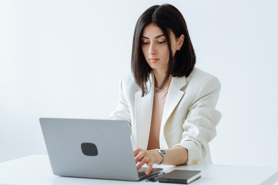 woman wearing a white work suit typing on a laptop - ways to be more productive 