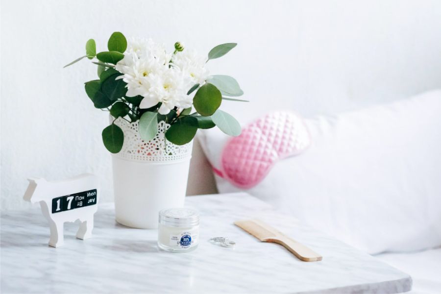 flowerpot, lotion bottle, table clock, and a comb on white table - things you need to create a daily routine