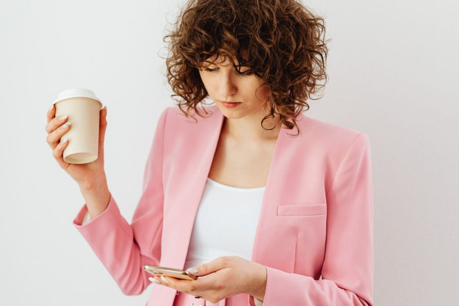 woman in pink blazer holding coffee mug, typing on her phone about habits of successful people