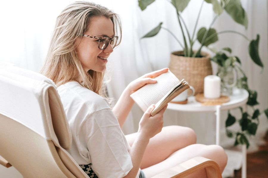 woman sitting in chair reading book during her summer morning routine