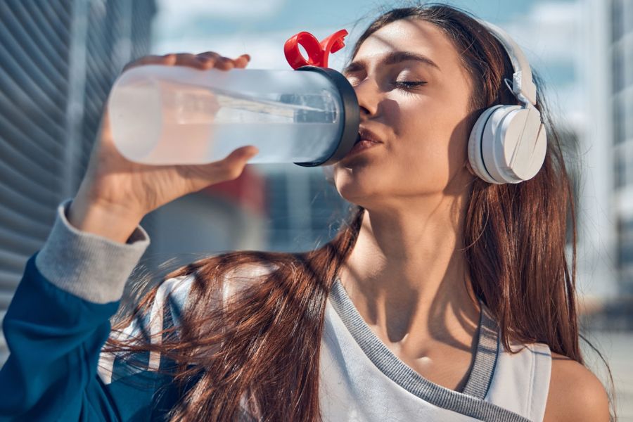 woman wearing headphones chugging water from a bottle