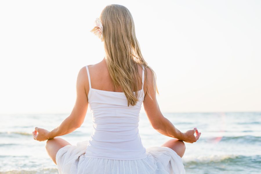 woman in white dress meditating at the beach