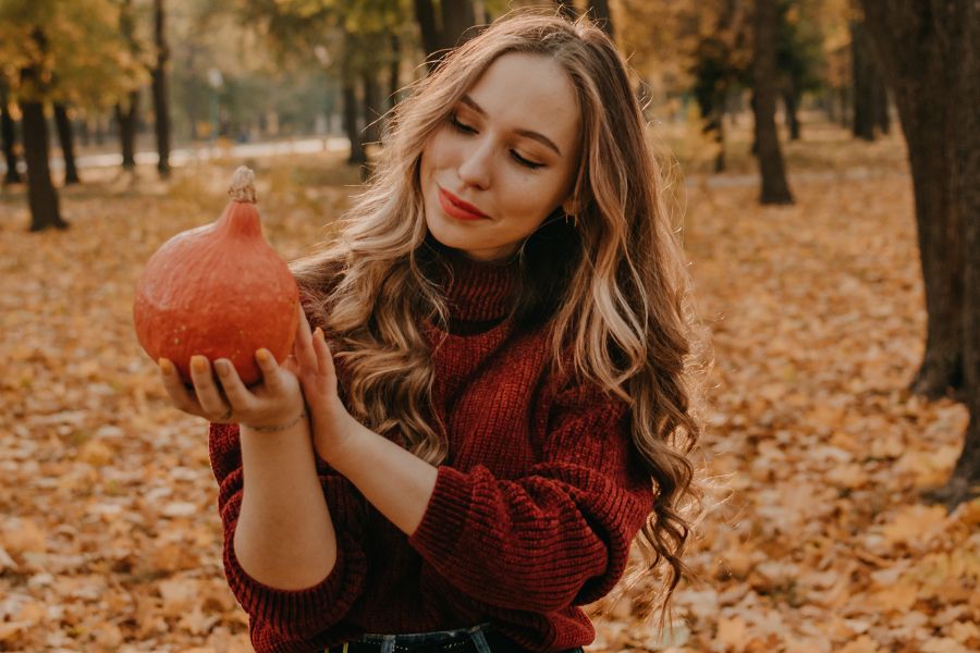 woman surrounded by fall leaves holding a tiny pumpkin