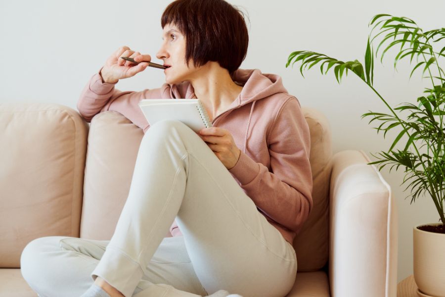 woman sitting on sofa thinking while journaling