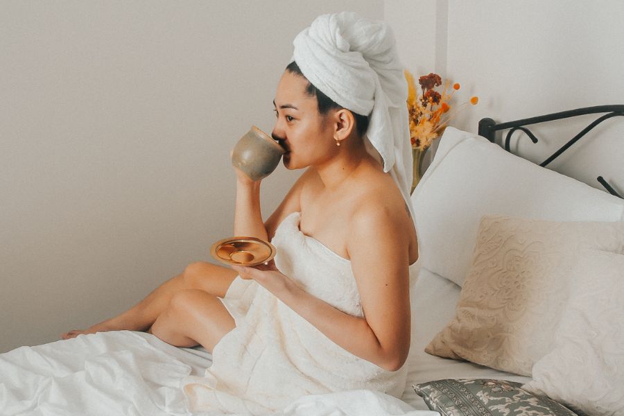 woman on bed sipping tea in morning in a bath towel