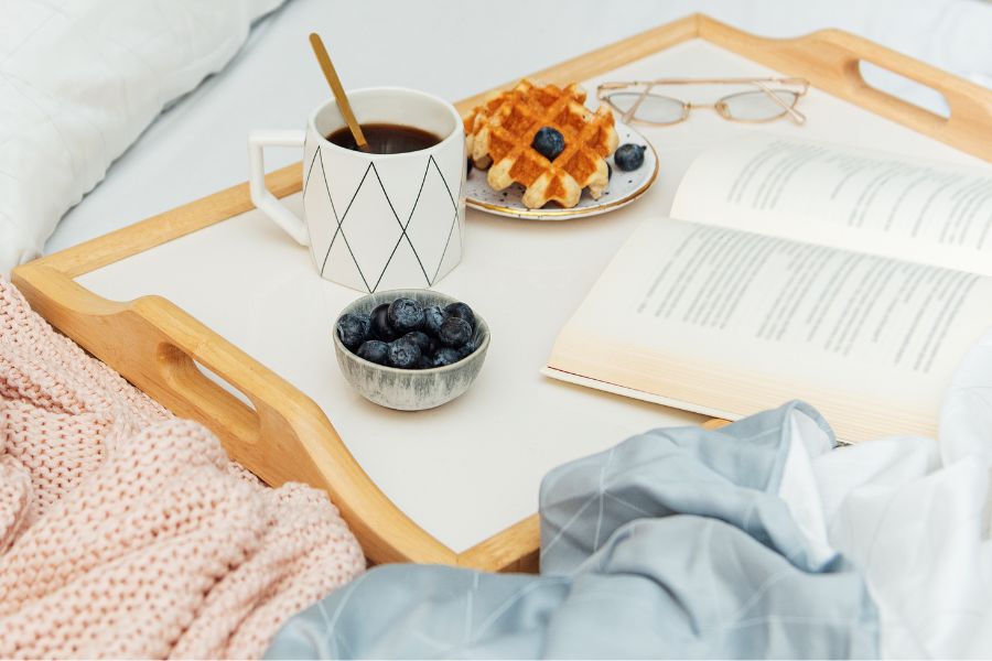 a breakfast tray carrying coffee, blueberries, a waffle, and a book