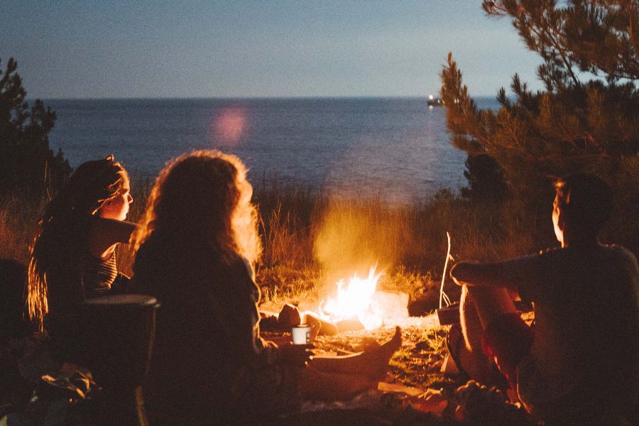 three friends sitting at bonfire at night near sea on beach