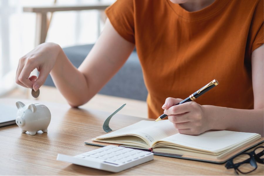 woman writing down investment plan in a diary with a pen, while putting a dollar in a guinea pig