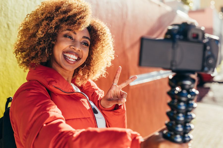 woman in orange jacket and curly hair vlogging as a side hustle