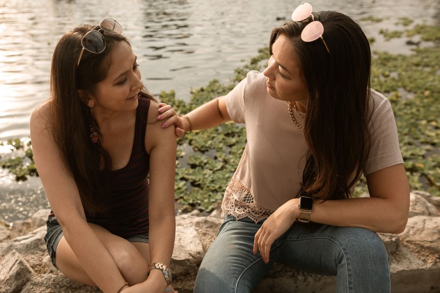 two women sitting by the lake talking to each other