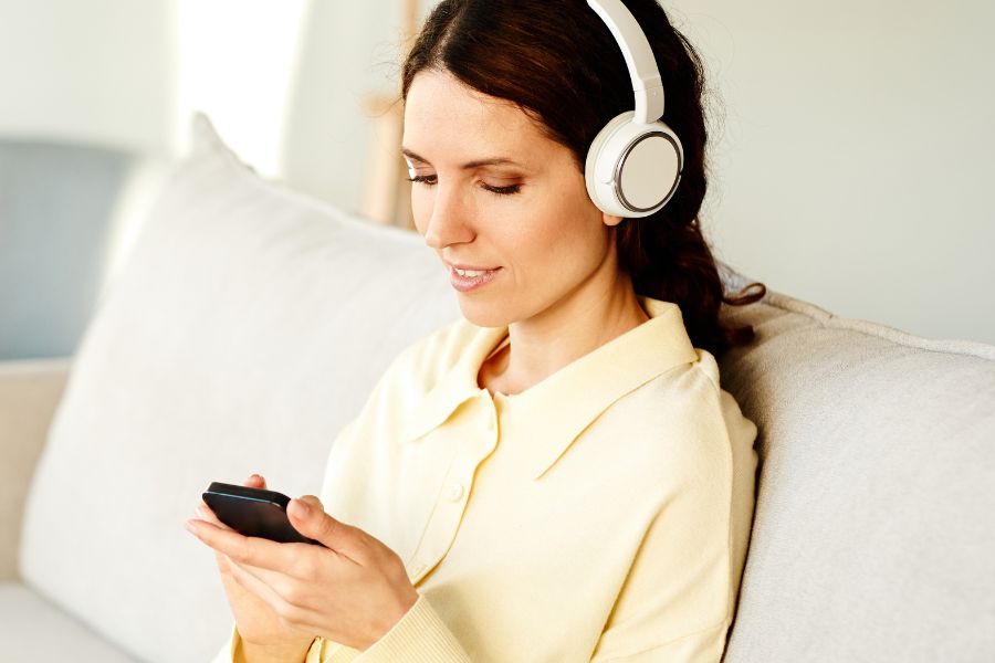 woman in yellow shirt wearing white headphones, doing something on phone