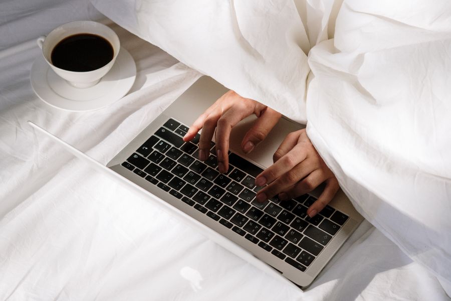 typing on laptop with coffee cup on bed