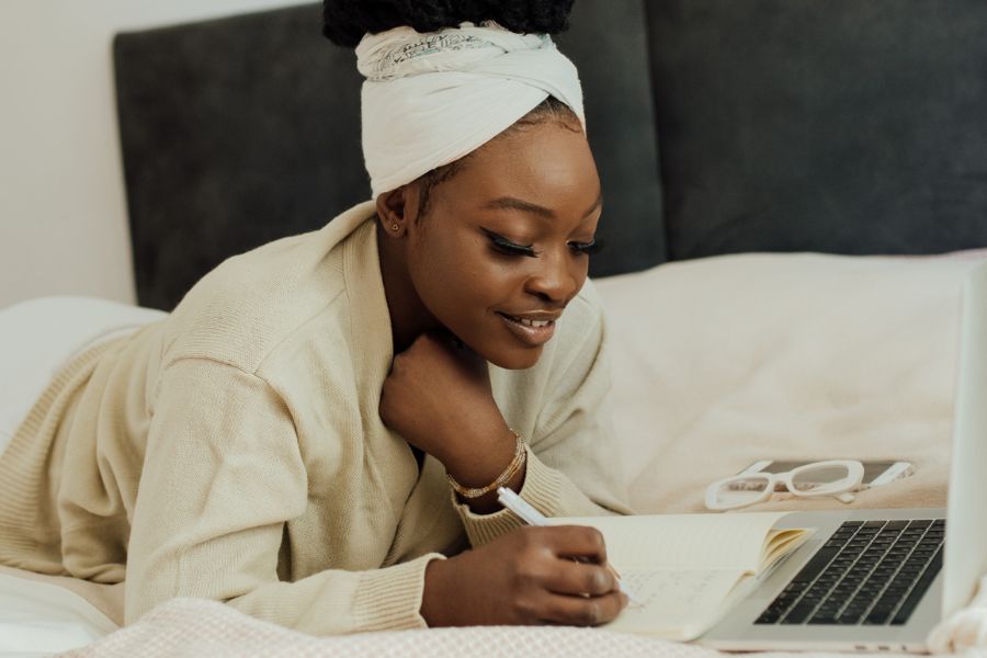 woman journaling in bed with laptop in front