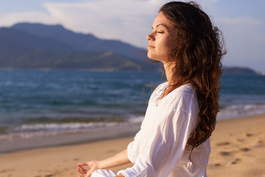 woman meditating on beach with eyes closed