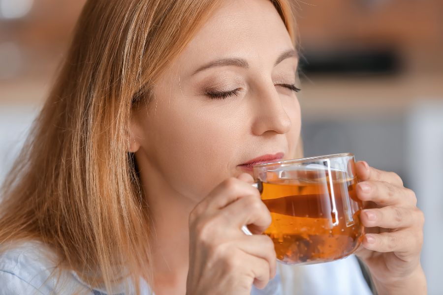 woman drinking tea in a clear cup with her eyes closed