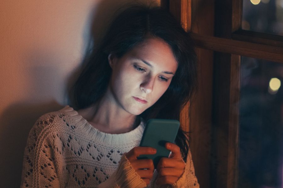 sad woman texting on phone with her head against the windows