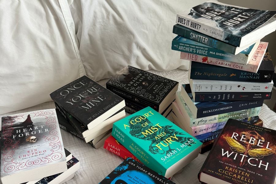 books lying on bed, like 'heart forger' 'once you're mine', 'a court of mist and fury' and 'rebel witch'