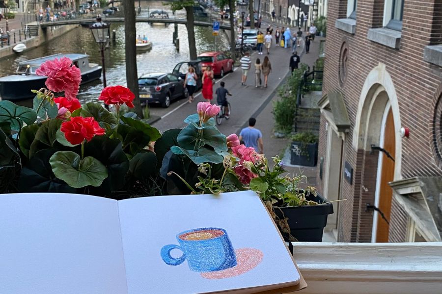 a drawing of a simple coffee mug on a blank journal placed on a balcony sill, overlooking a city view