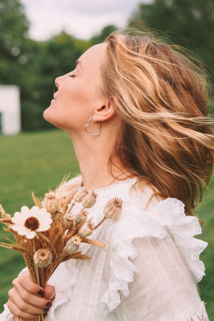 woman feeling breeze on face with eyes closed, holding wild flowers in hand