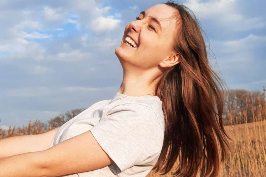 woman laughing freely with eyes closed, hair blowing behind, standing in a corn field