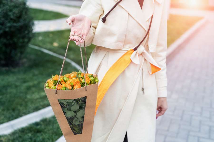 hand carrying orange flowers in a. cardboard container
