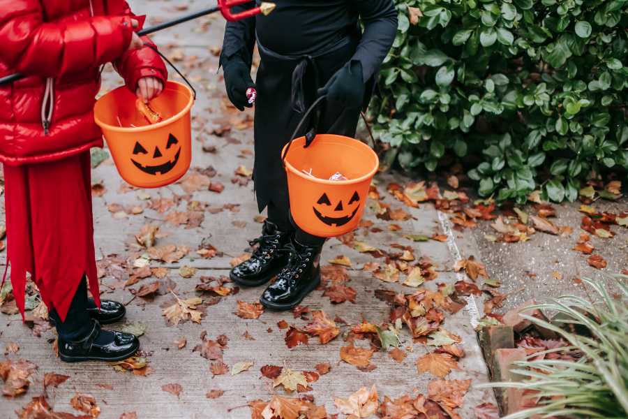 feet of two kids visible holding pumpkin buckets with candies