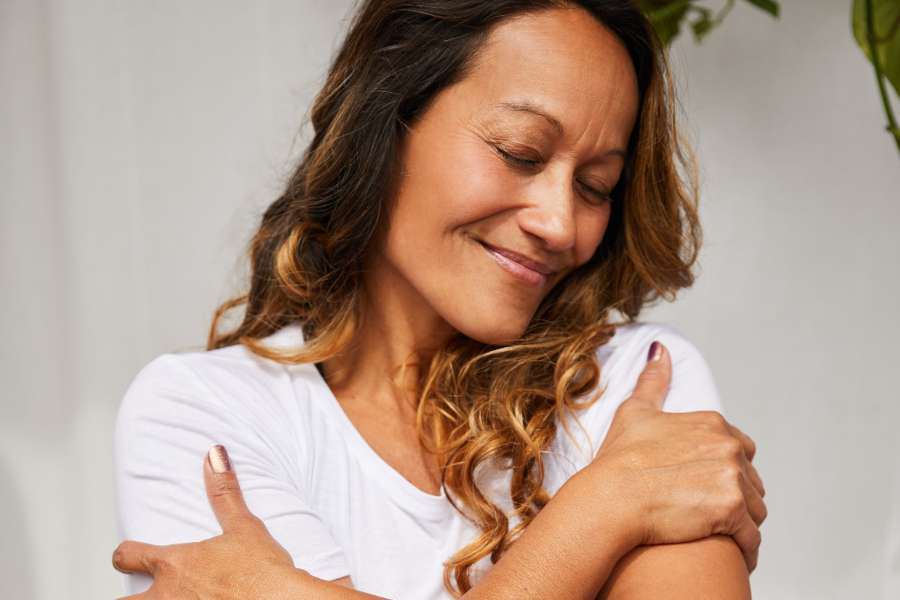 smiling woman hugging herself with eyes closed