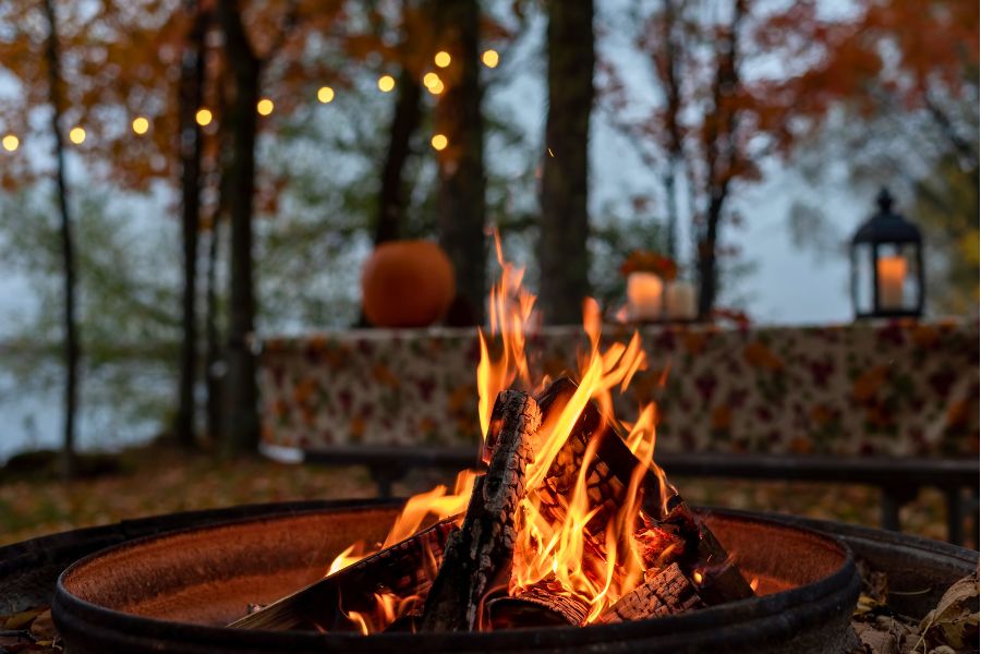 bonfire burning in an autumn setup with fairy lights and pumpkin behind