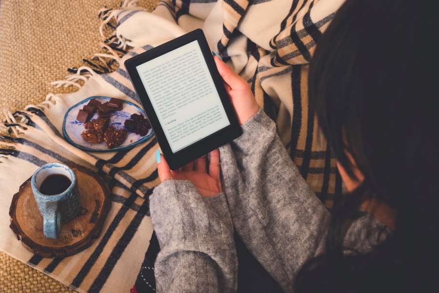 woman reading on kindle with coffee and cake in plate