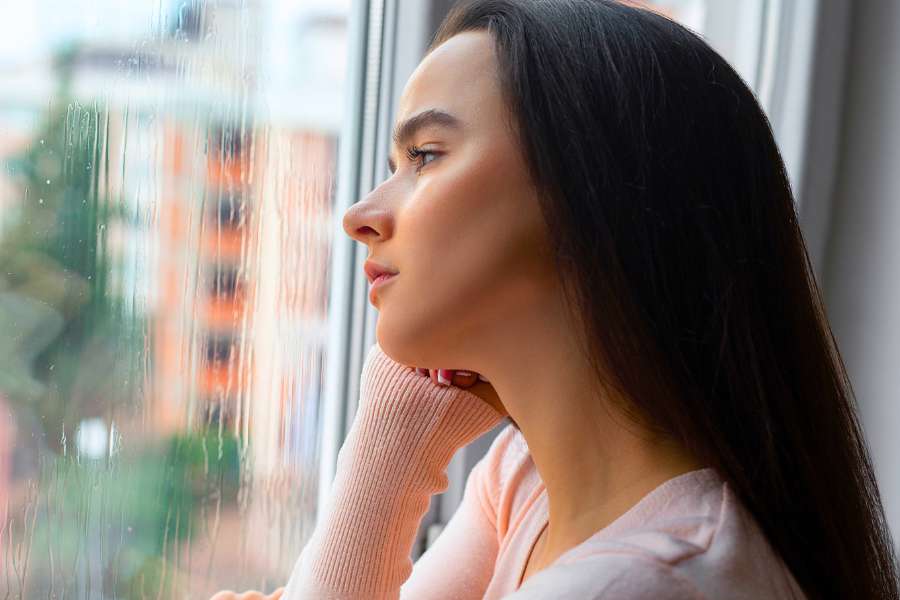 woman with chin in hand staring out window while it's raining outside