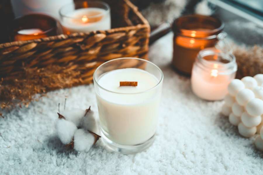 a white scented candle on a furry table, surrounded by blurred lit-up candles