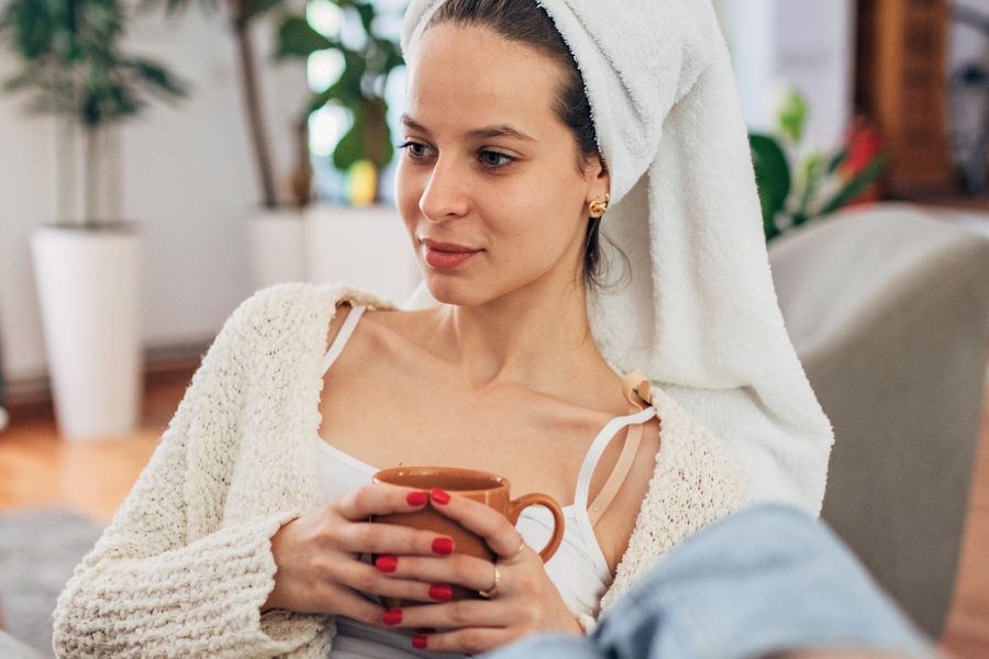 woman with head wrapped in towel holding a mug, looking at nothing with a smile 