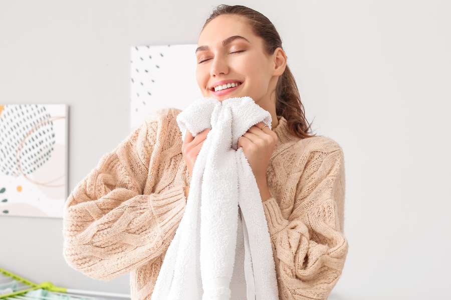 woma wearing beige sweater hugging a white towel with her eyes closed and a smile on face