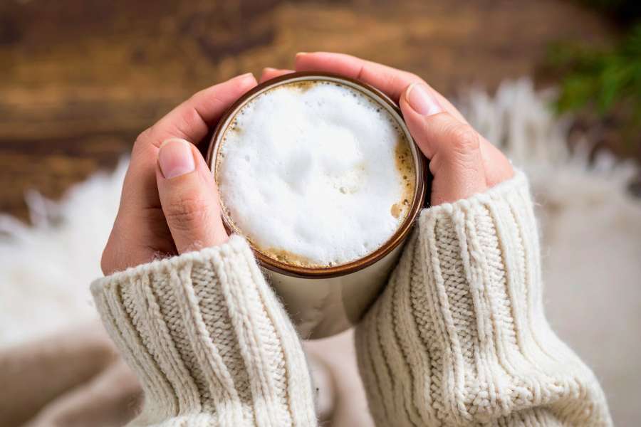 holding a mug of frothy coffee in hand