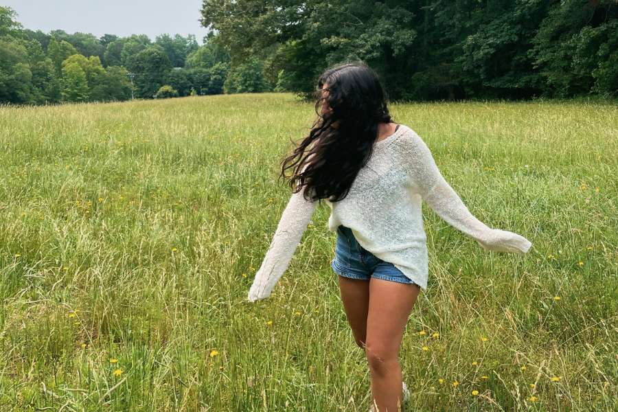 woman in a sheer sweater and denim shorts, twirling in a field with hair covering her face