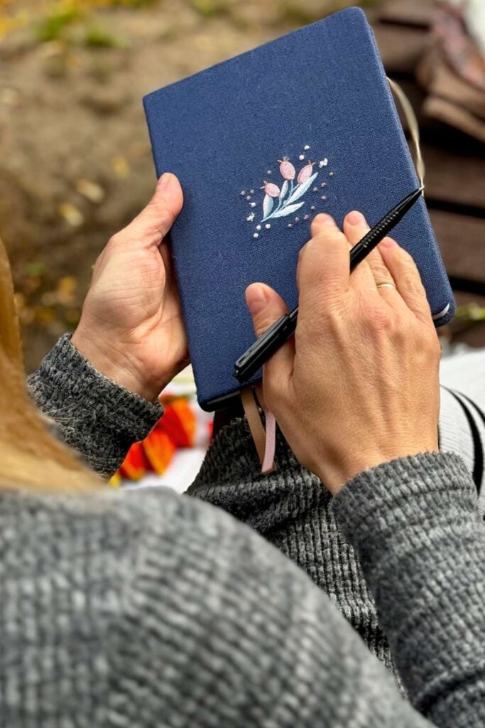 hands holding a blue journal and a black pen